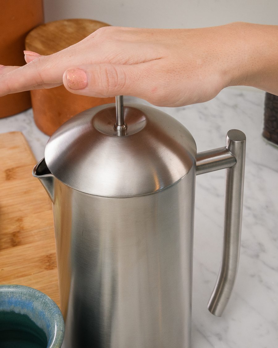 A hand pressing the plunger on the brushed Frieling French Press